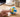 A hand gently squeezing a white, blue and yellow paneled volleyball-style silicone squishy on a home desk in soft morning light.