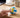 A hand gently squeezing a white, blue and yellow paneled volleyball-style silicone squishy on a home desk in soft morning light.